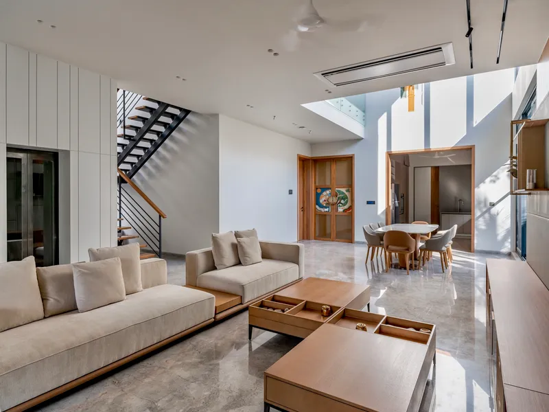 Double-height living space with skylight above steel staircase casting sharp shadows on white walls