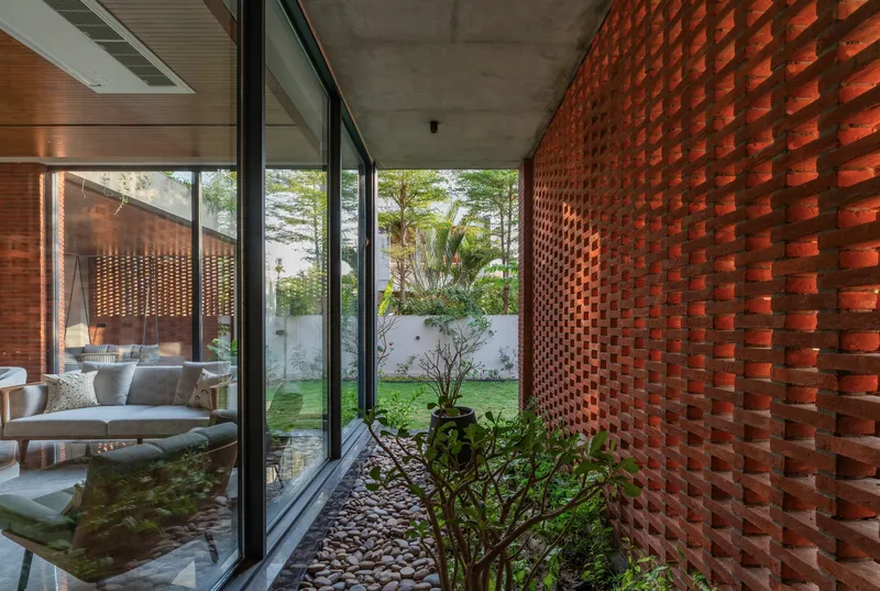 Covered passage with perforated red brick wall alongside a planted courtyard with shrubs and pebbles