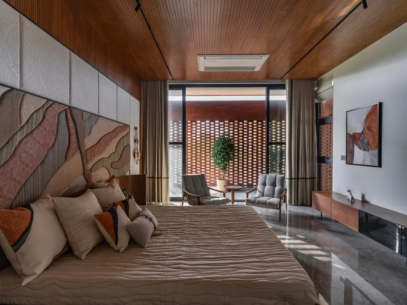 Bedroom with timber slatted ceiling looking through glazed doors toward a perforated brick screen in daylight