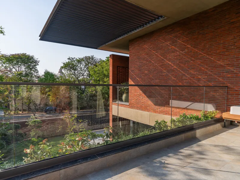 Upper terrace with glass balustrade overlooking a planted courtyard with red brick volumes beyond