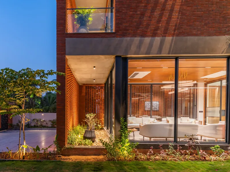 Exterior corner illuminated at dusk showing perforated brick entry and full-height glazing with interior lights