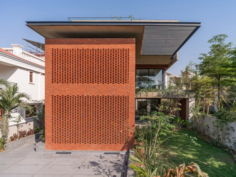 Perforated brick screen wall rising three stories with broad horizontal roof overhang and garden below