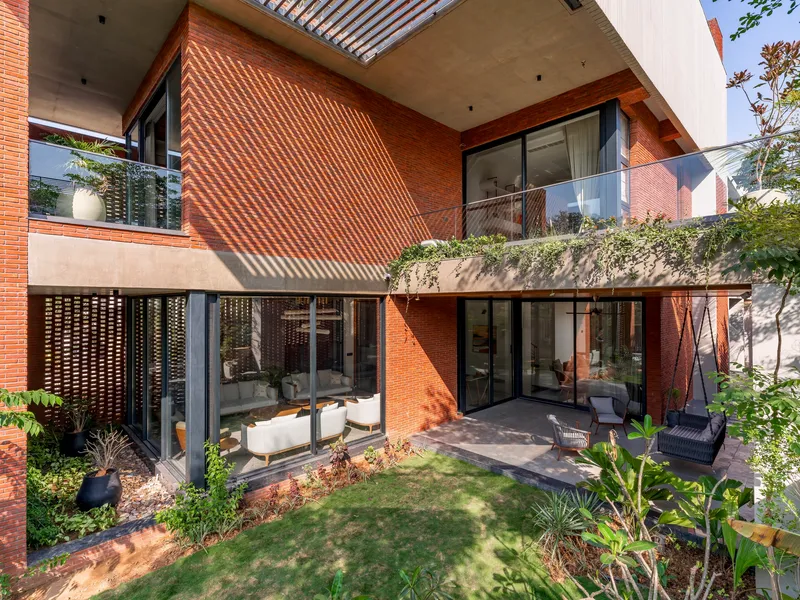 Rear courtyard with glass walls, planted balconies, and brick screens casting shadow patterns