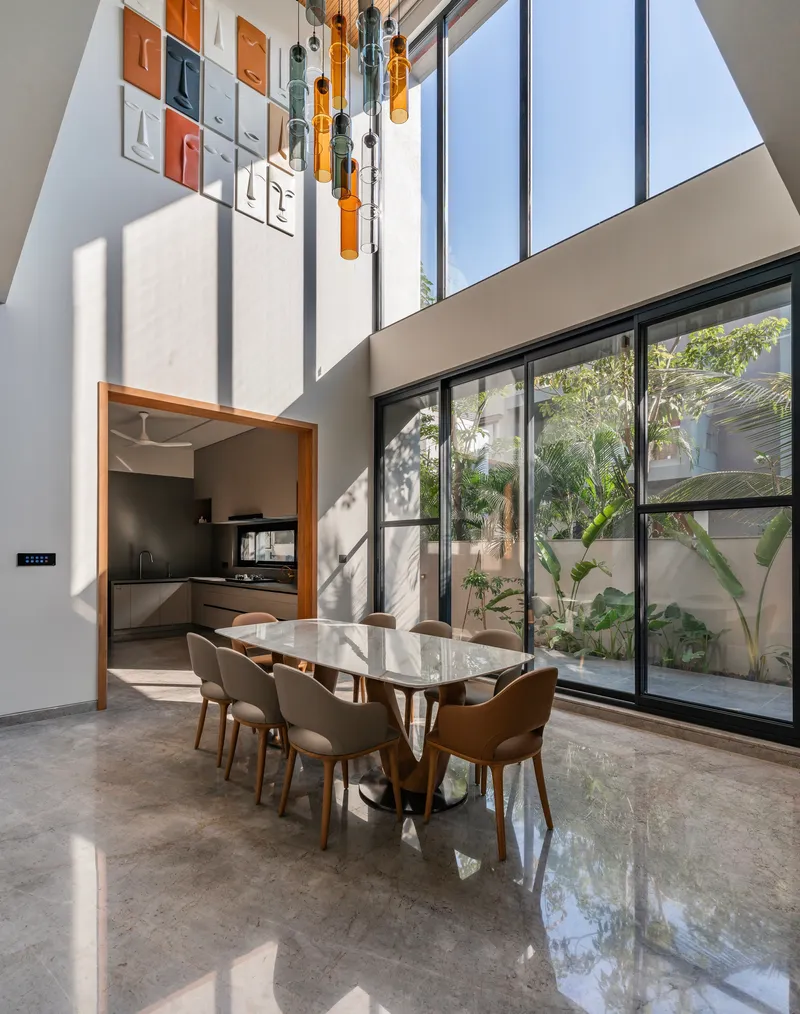 Double-height dining area with pendant lights and full-height glazing flooding polished floors with sunlight