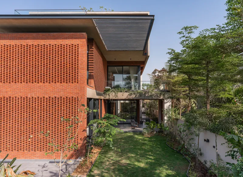 Two-story perforated brick screen wall beside planted lawn with mature trees in background