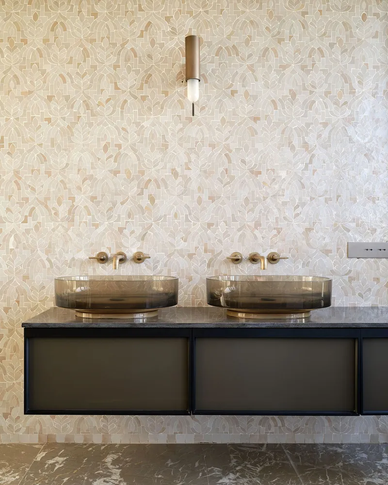 Floating vanity with smoked glass vessel sinks and brass fittings against geometric patterned mosaic tile wall