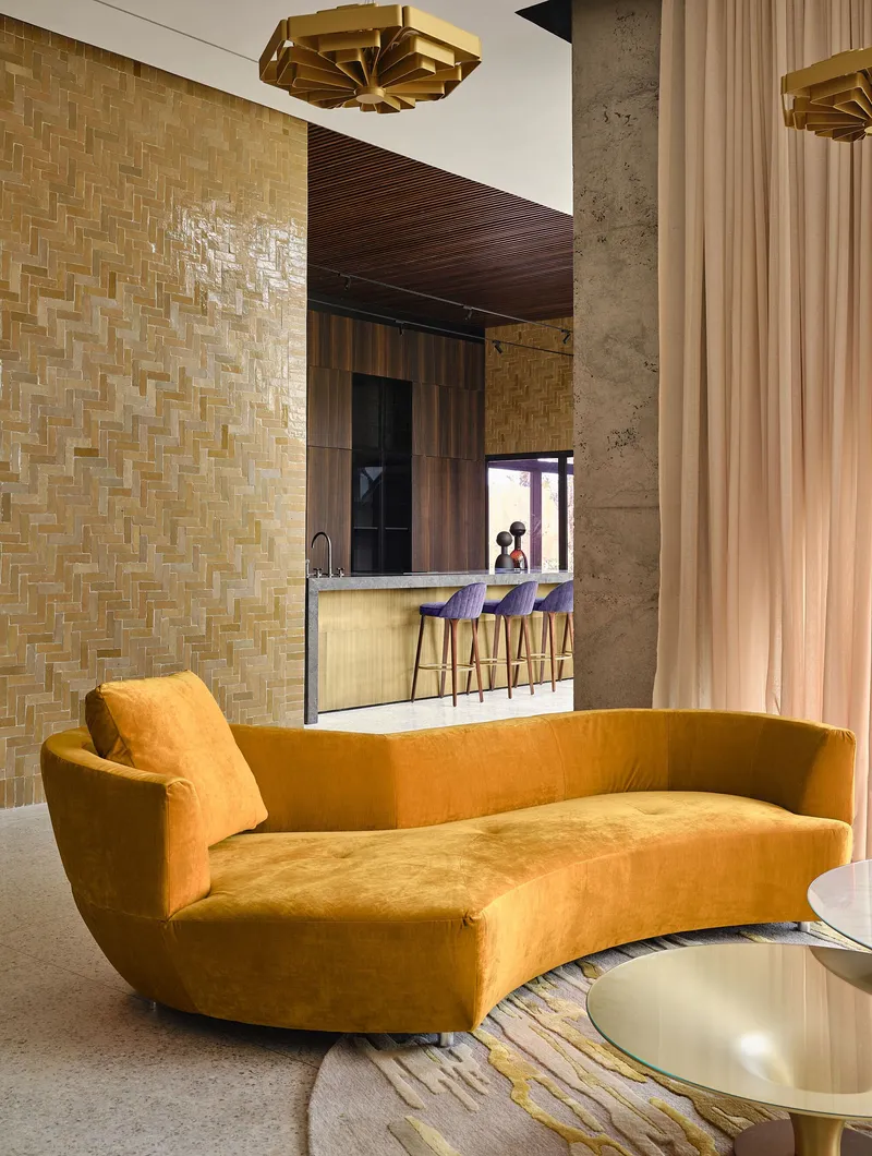 Living area with curved sofa facing basketweave tile wall and bar seating beneath ribbed timber ceiling