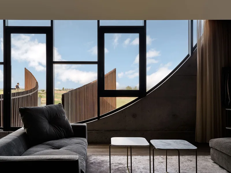 Interior sitting area with floor-to-ceiling windows framing slatted timber screens and distant landscape under blue sky