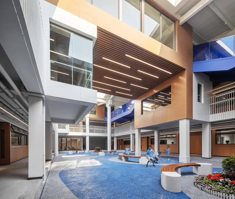 Multi-story atrium with timber-slat ceiling, blue carpet flooring, and curved seating where students gather