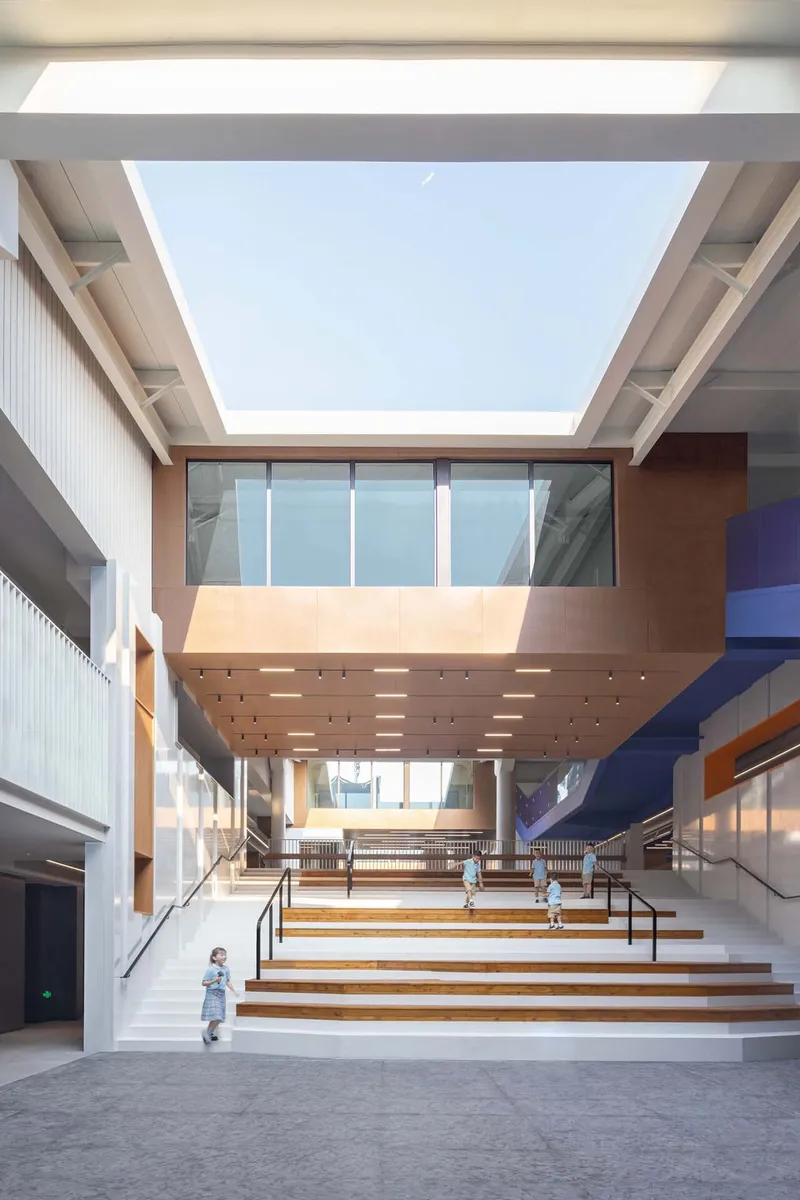 Wide interior staircase with timber treads ascending beneath a perforated ceiling and skylight overhead