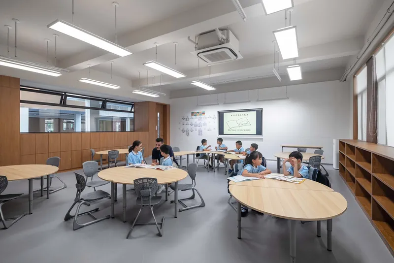 Classroom with oval tables, suspended linear lights, and students working in small groups