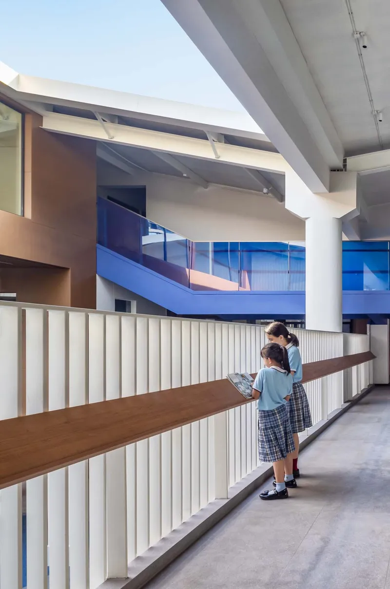 White slatted balustrade with timber handrail where two students lean and read overlooking an atrium