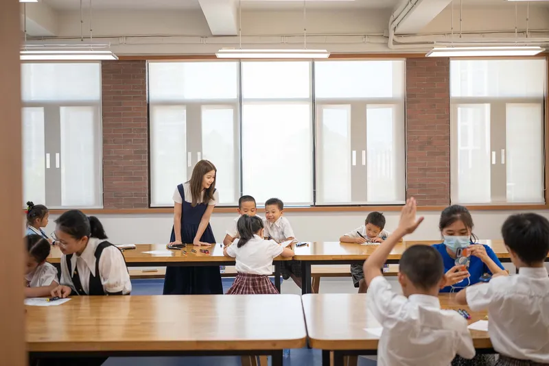 Classroom with large gridded windows and exposed brick piers where students work at wooden tables