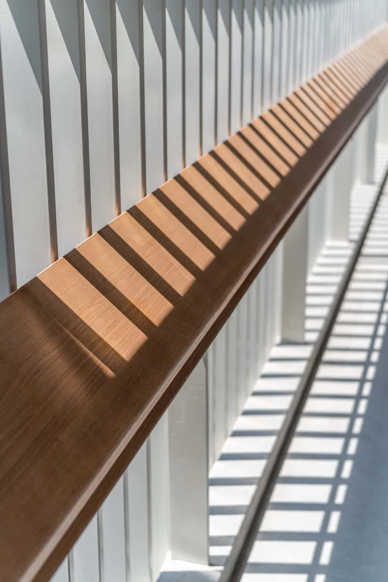 Timber handrail with slatted shadow pattern cast by vertical louvres in bright sunlight