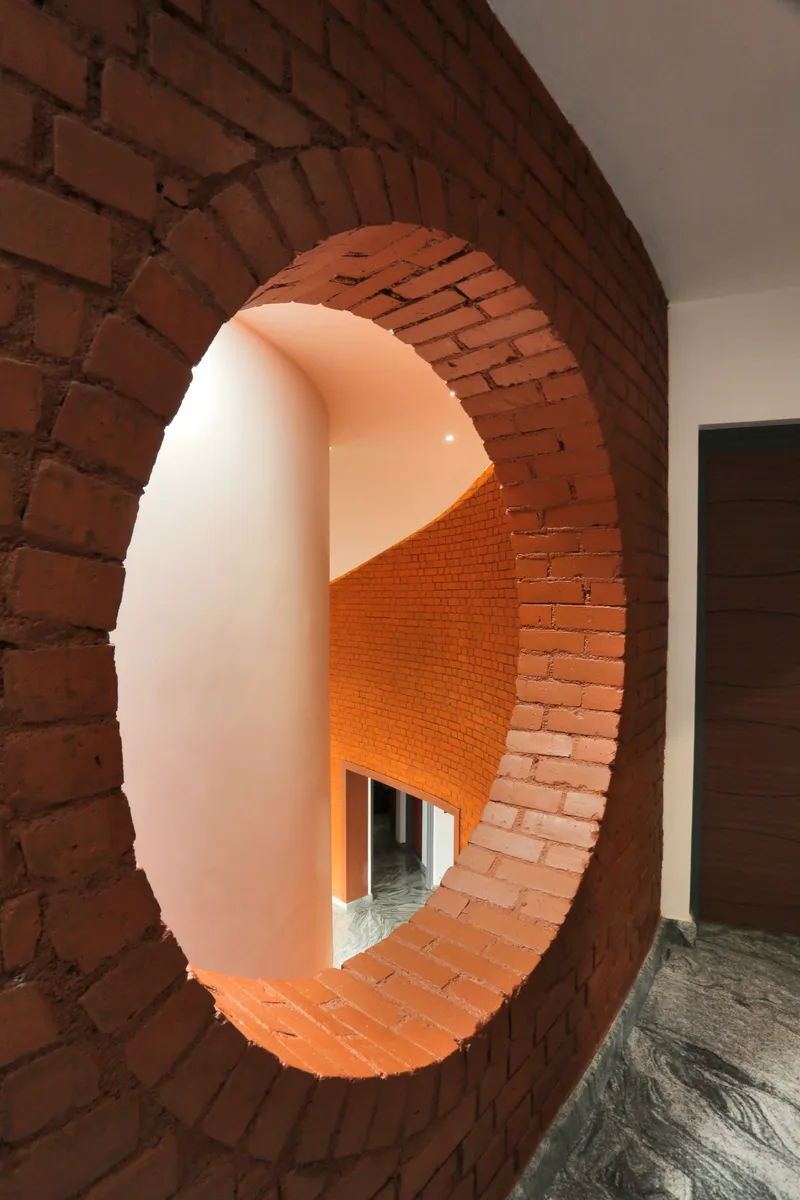 Circular brick opening framing a view through to a curved stairwell with warm artificial lighting