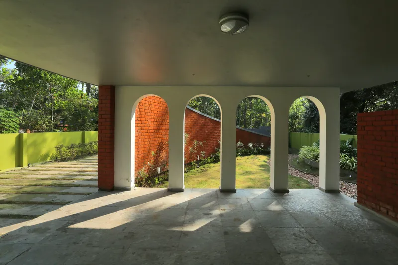 Covered porch with arched openings framing a garden courtyard with planted beds and brick walls in daylight