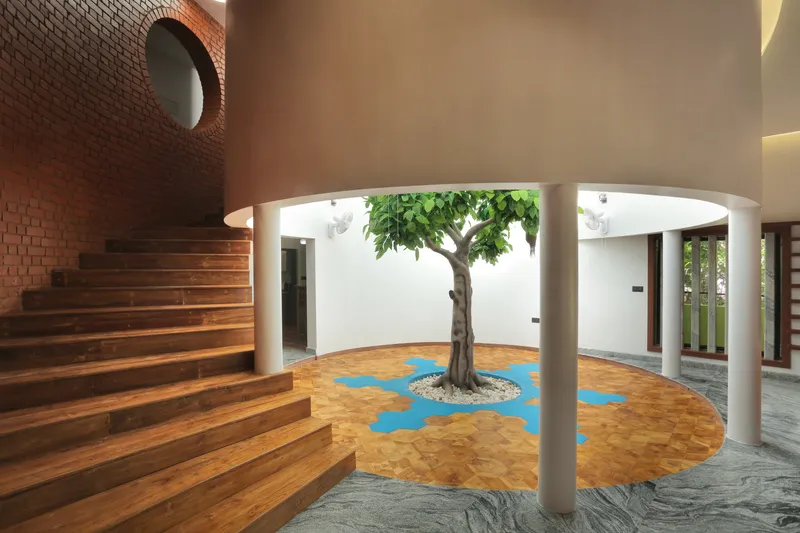 Interior courtyard with a planted tree set in parquet flooring with blue inlay beneath a curved skylight