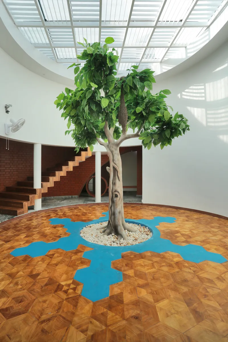 Interior tree in the central courtyard beneath a slatted skylight casting dappled shadows across parquet floor