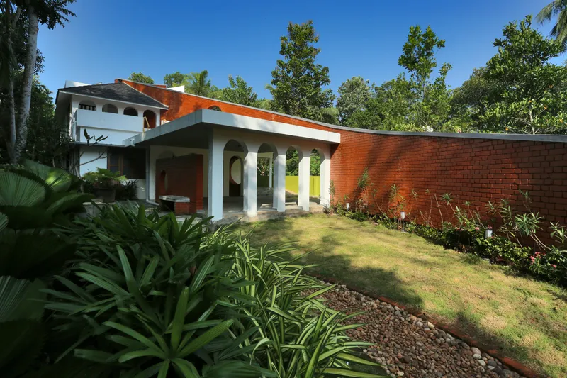 Garden view of the red brick boundary wall and covered colonnade framed by tropical plantings