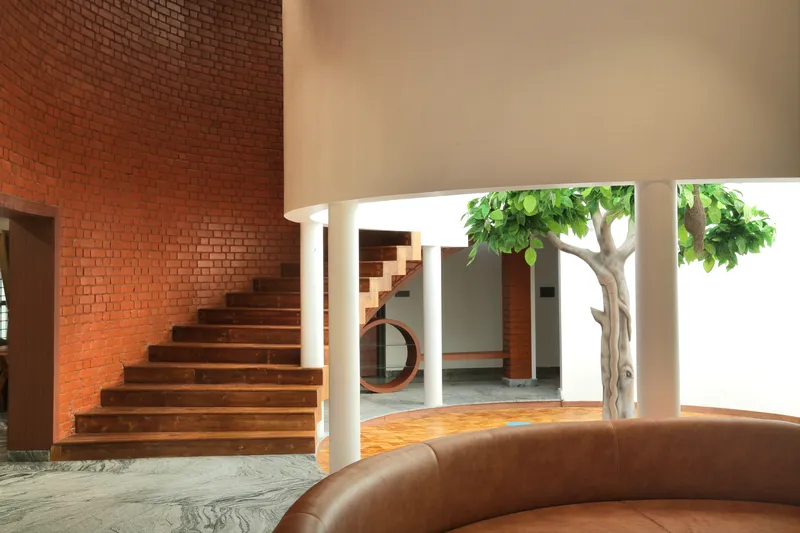 Interior staircase with timber treads against a red brick wall opening to a courtyard with a potted tree