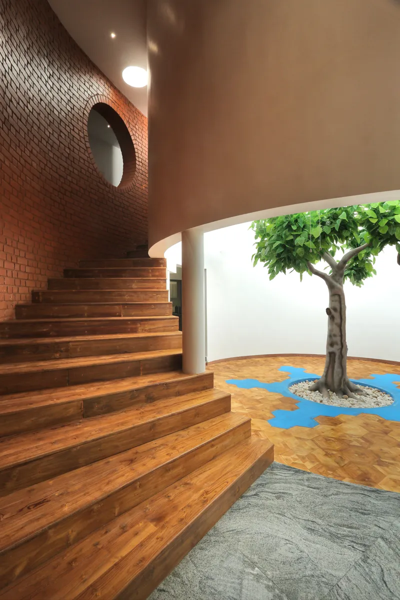 Timber stair rising along the curved brick wall beside a courtyard with tree and patterned floor inlay