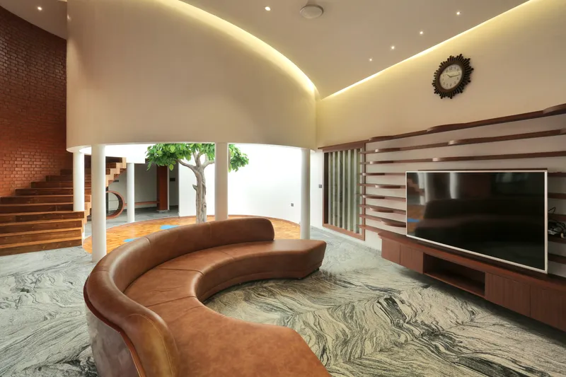 Living area with curved leather sofa beneath a vaulted ceiling lit by concealed perimeter lighting