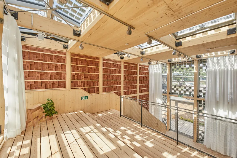 Upper-level space with red brick storage wall and planted bench lit by skylights