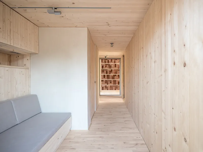 Narrow corridor with plywood walls framing a view to the brick wall beyond