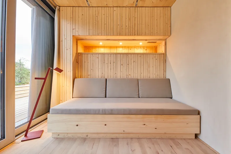 Sleeping alcove with plywood bed and recessed lighting beneath a timber ceiling