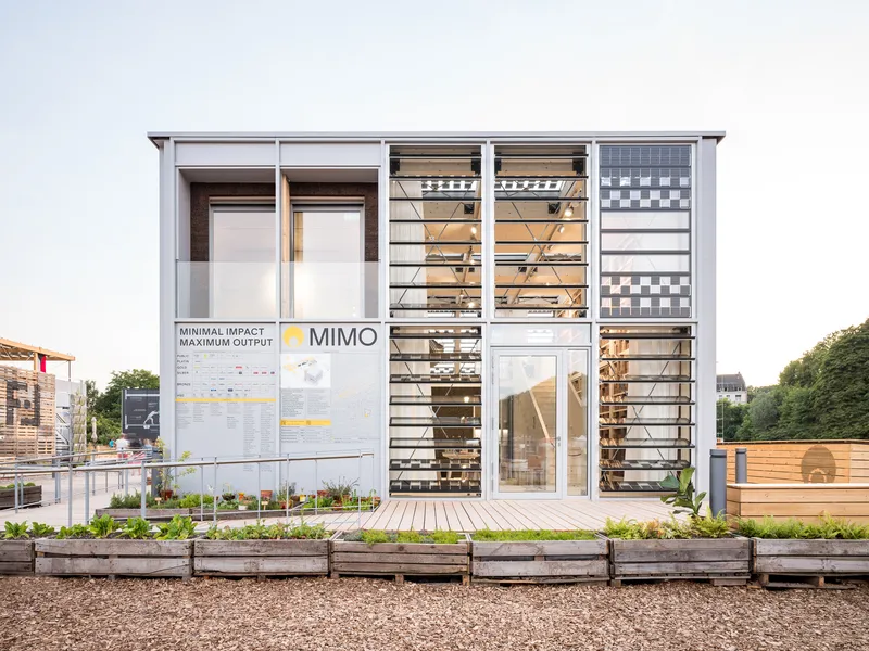 Facade showing louvered upper windows and informational panels beside raised planter beds in afternoon light
