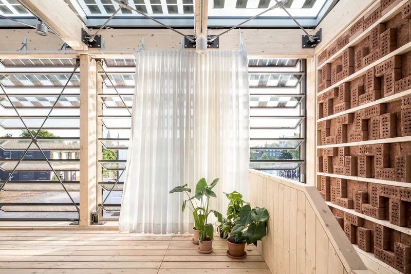 Interior upper level with light wood flooring, perforated brick wall and white curtain divider under skylights