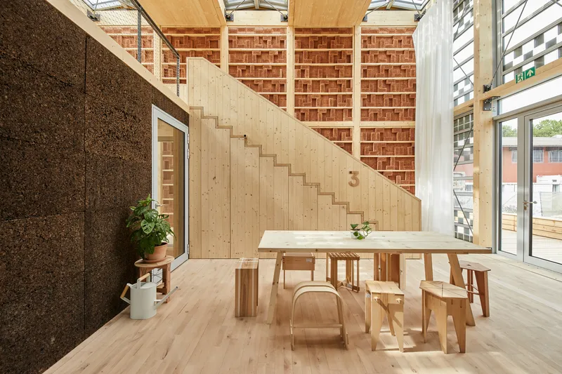 Diagonal staircase in light timber against cork wall with simple wood furniture and overhead glazing