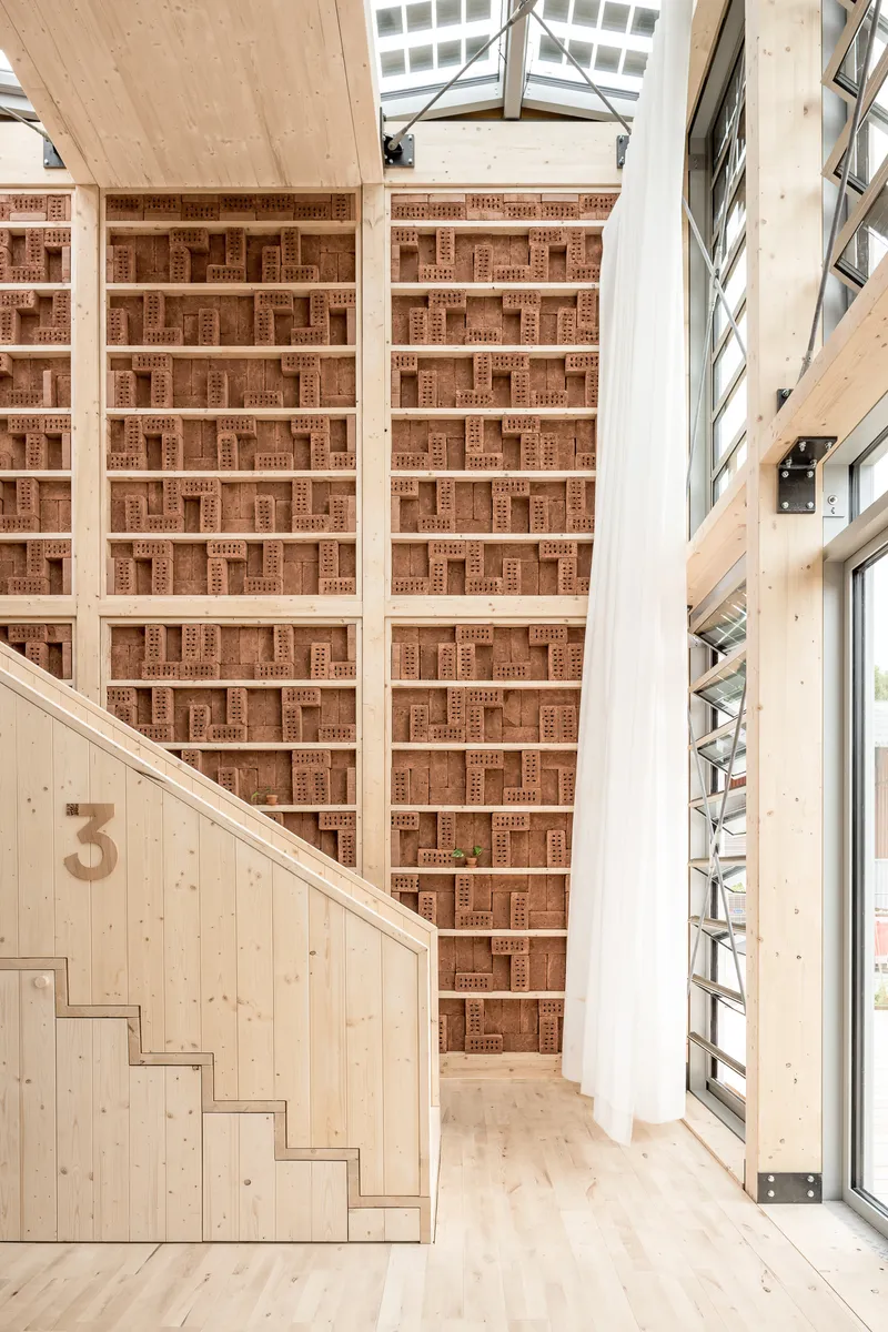 Double-height space with perforated brick wall, timber staircase and triangular glazed clerestory above