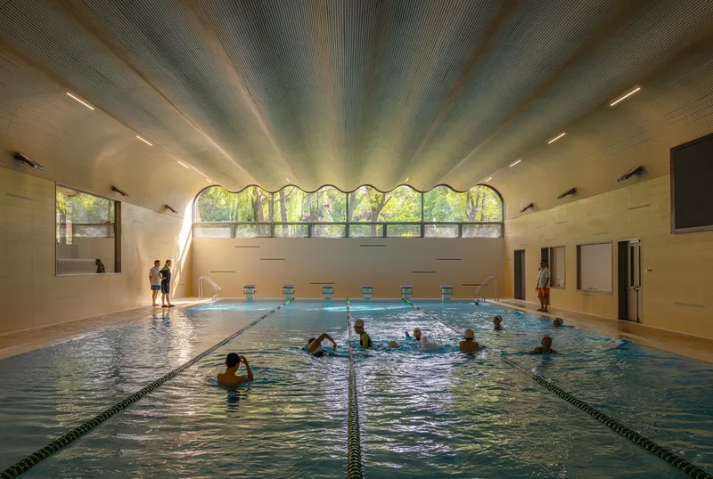 Indoor swimming pool with arched clerestory windows and timber ceiling beams illuminated by natural light