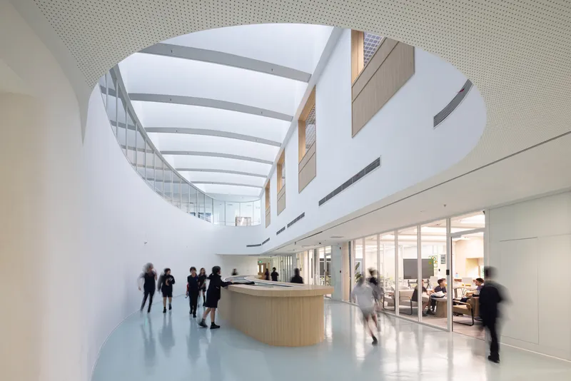 Oval skylight above a curved reception desk with people moving through the daylit lobby space
