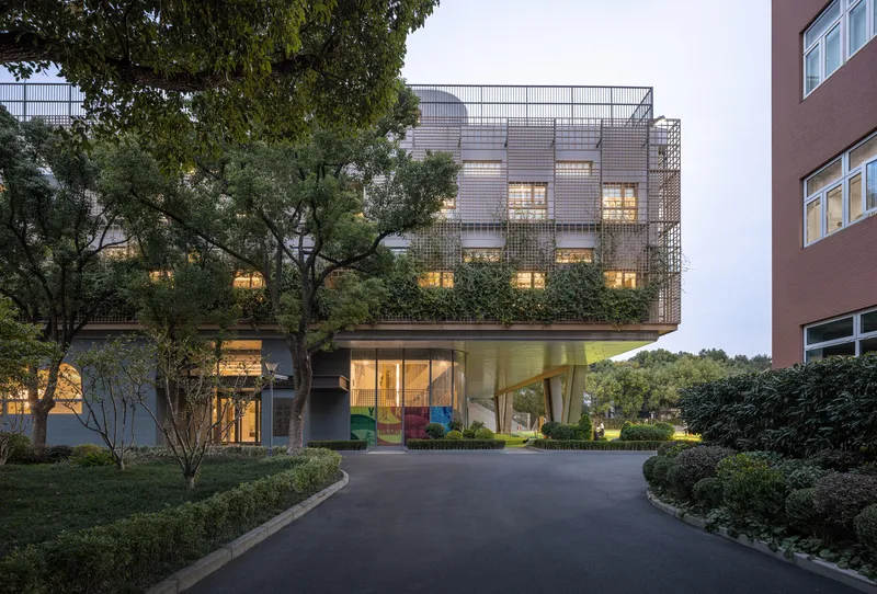 Elevated building with perforated metal facade and underlit cantilevered volume at dusk