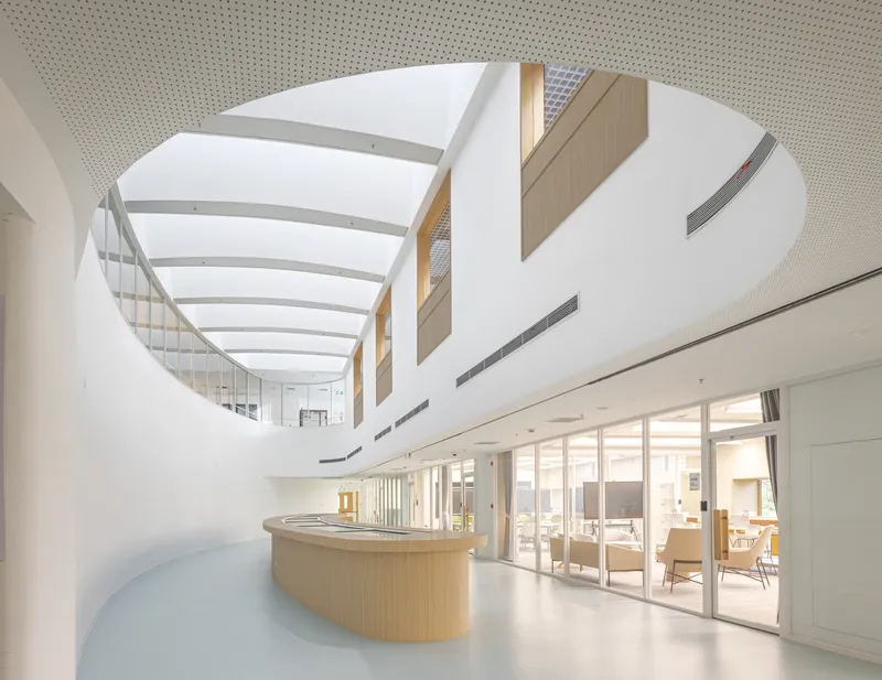 White atrium with curved timber reception desk and skylight ribs overhead
