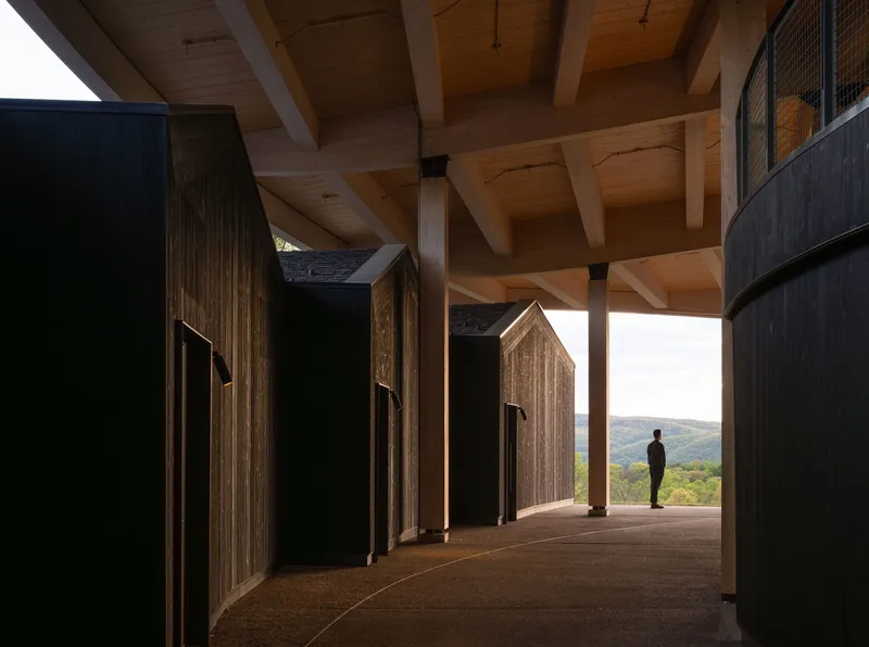 Sheltered passage with timber-clad house-shaped volumes under exposed beam ceiling and mountain view