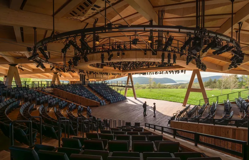 Interior amphitheater showing curved seating tiers, circular lighting rig, and timber stage under laminated wood ceiling