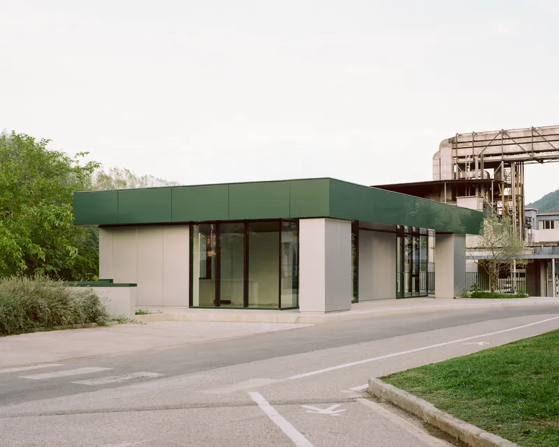 Corner elevation showing the cantilevered green roof and glass entrance with an industrial facility behind