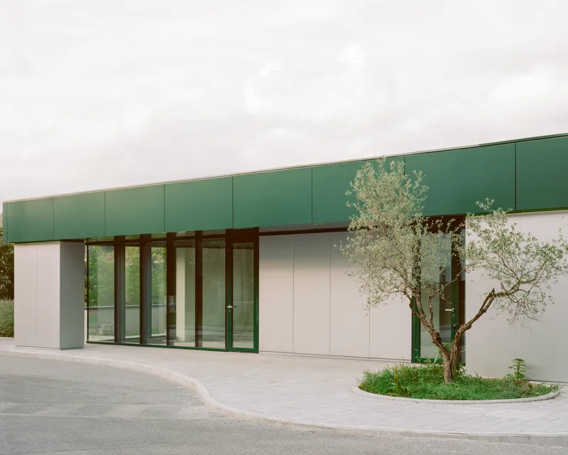 Facade detail of the glass entrance wall with white panels and olive tree in circular planter bed