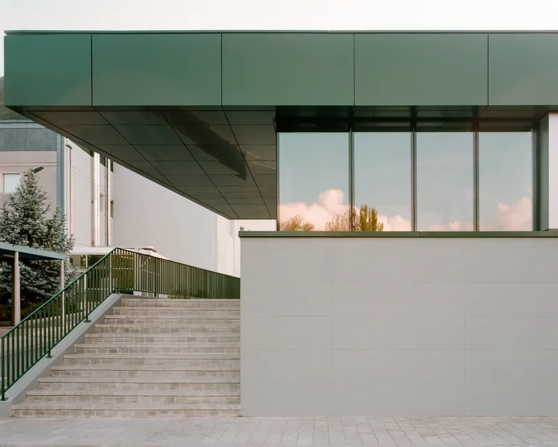 Covered stairway with green metal railings leading up beneath the cantilevered roof at dusk