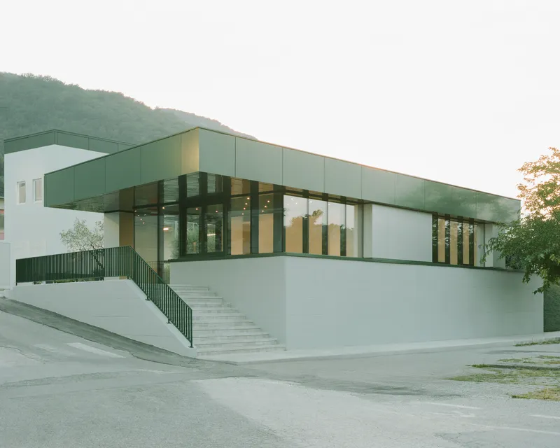 Corner view of the elevated entrance plaza and glazed facade with forested hillside behind
