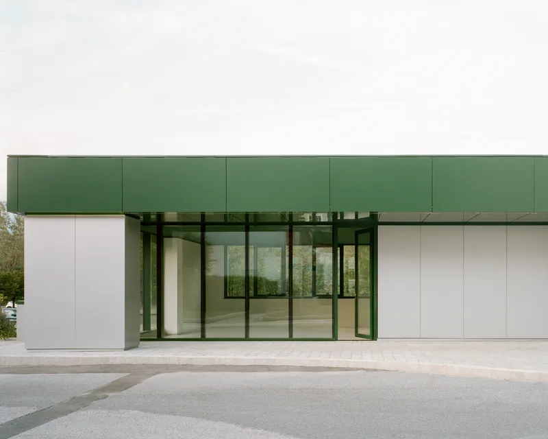 Recessed glass entry portal framed by white panels and green metal canopy under overcast sky