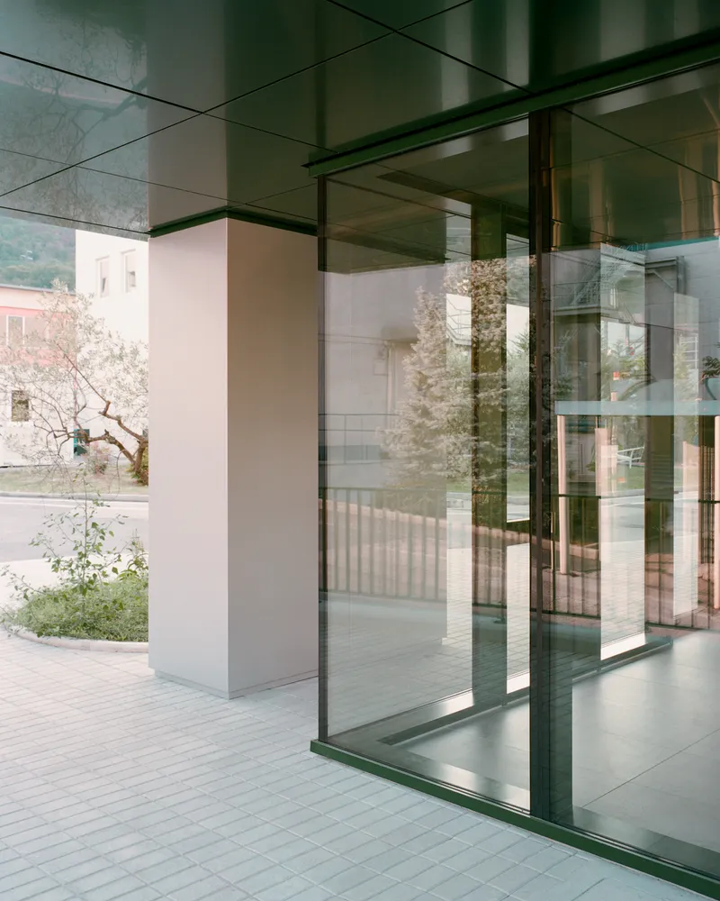 View through glass facade showing layered reflections of courtyard trees and adjacent building volumes