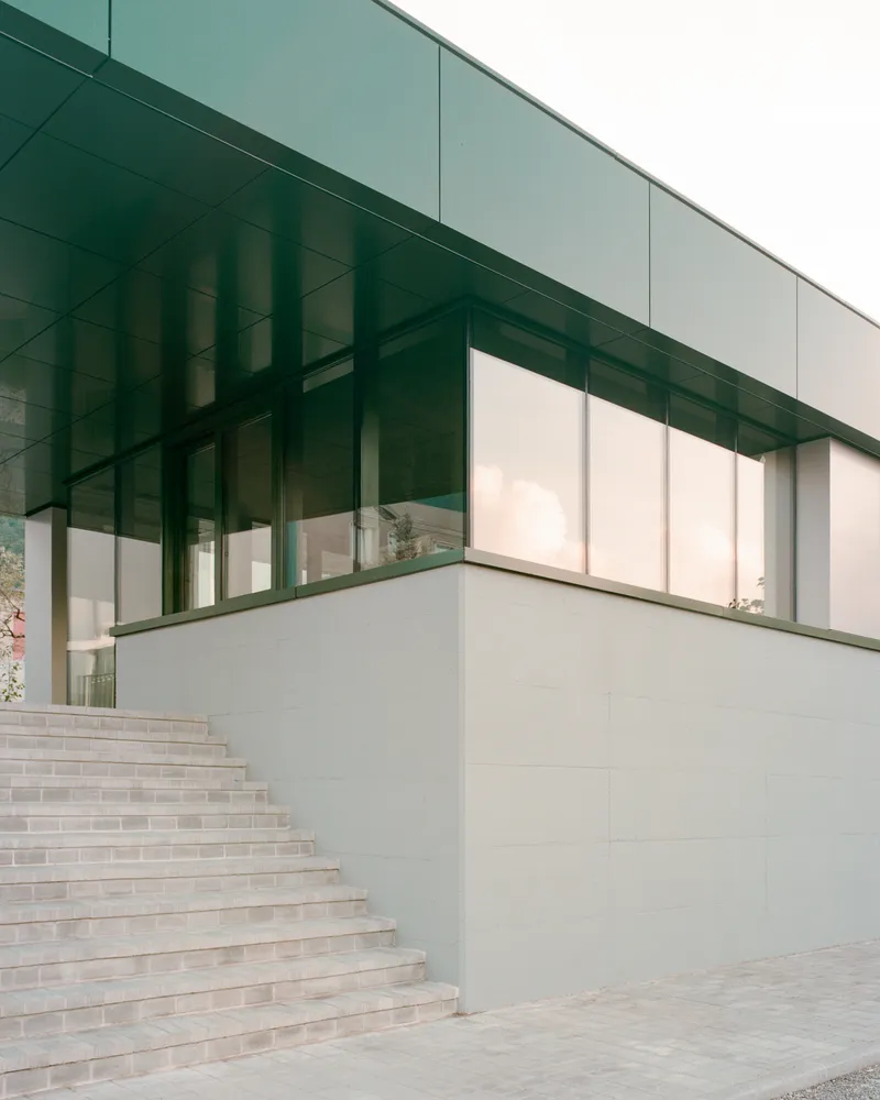 Exterior staircase ascending alongside corner glass volume with green metal soffit above
