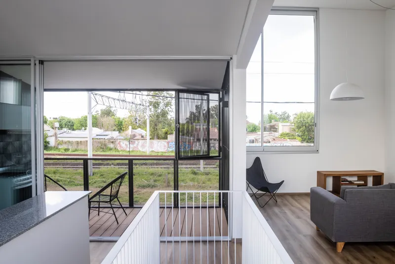 Interior living space opening to a timber deck through floor-to-ceiling glass with perforated metal screens beyond