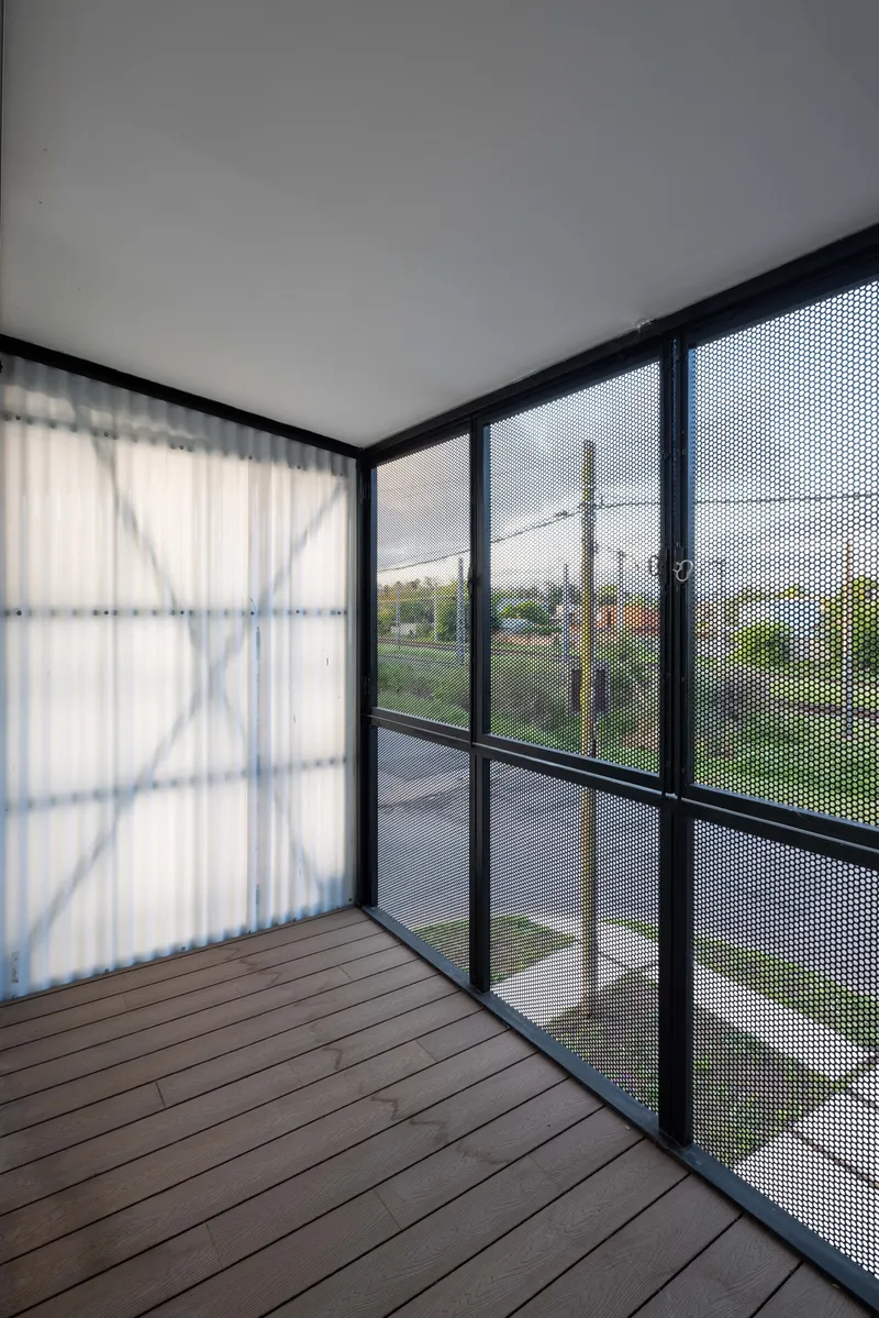 Balcony with timber decking enclosed by black-framed perforated mesh screens overlooking a suburban street