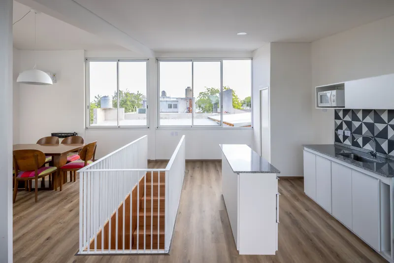 Open kitchen and dining area with white vertical slat stair guard and full-width windows overlooking rooftops