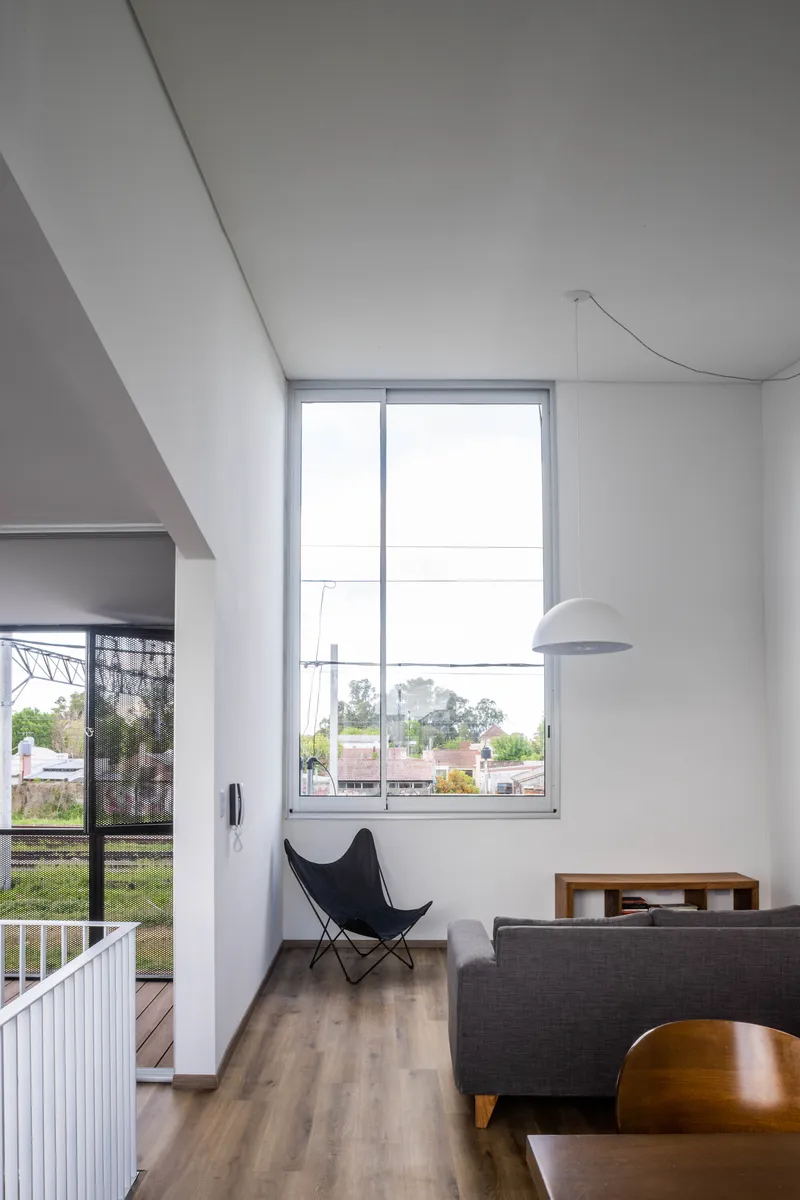 Double-height living area with sloped ceiling and tall window framing view of suburban rooftops